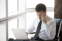 headaches and migraines - man sitting at computer hand on forehead